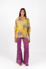 Camisa de manga larga con cuello clásico y cierre frontal de botones, confeccionada en tejido de color verde lima con estampa floral en tonos morados y naranjas.