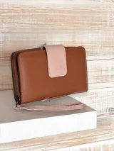 Billetera grande de cuero color marrón con solapa rosa y cierre de cremallera. Incluye correa de mano extraíble.