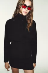 Vestido corto de punto con cuello subido, manga larga y sisa ancha. Presenta un detalle de costura vertical marcada en el centro del delantero y acabados en rib en cuello, puños y ruedo.