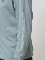 Remera de manga larga en color verde azulado, con corte regular fit. Presenta un estampado cuadrado en la espalda con una X grande y detalles de marca en la manga.