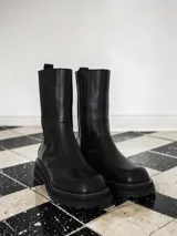 Bota de caña media confeccionada en cuero, con elásticos laterales y suela track con costura a la vista.