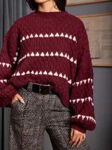 Buzo de tejido de punto en color bordó, con diseño de rayas horizontales formadas por pequeños triángulos blancos. Presenta cuello redondo, mangas largas con puños ajustados y un corte holgado.