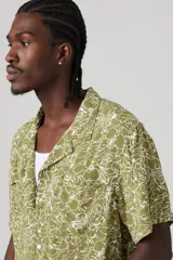 Camisa de manga corta color verde oliva con estampado floral blanco, cuello tipo camp y bolsillo en el pecho.