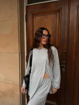 Conjunto de dos piezas color gris melange, confeccionado en tela de lanilla, compuesto por un buzo de manga larga con diseño cruzado al frente y un pantalón largo de corte holgado y tiro alto.