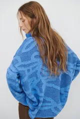 Buzo de tejido de punto con cierre frontal, cuello alto y diseño estampado en tonos beige y marrón.