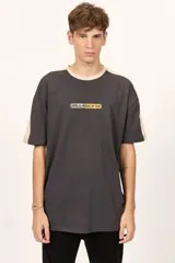 Remera oversize Billabong de color negro, con cuello redondo en tono beige y detalles de bandas beige en los hombros y mangas. Cuenta con un pequeño estampado frontal con el logotipo de la marca.