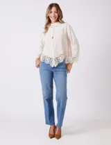 Camisa de algodón con bordado suizo, cuello con solapa y cierre frontal con botones. Presenta mangas largas con terminación de encaje calado y un ruedo asimétrico en pico con un amplio galón de encaje.