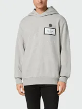 Buzo gris con capucha y cordones ajustables, de corte holgado y mangas largas. Presenta un parche rectangular con el logo de la marca en el frente y un pequeño logo hexagonal en la parte superior.