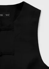 Chaleco negro de mezcla de algodón y lino, con cuello redondo, sin mangas, cierre frontal con botones de presilla y detalle de abertura en el bajo.