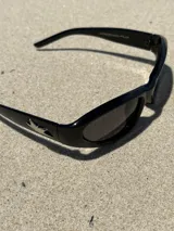 Gafas de sol negras con montura rectangular, lentes oscuras y detalle de estrella plateada en el lateral.