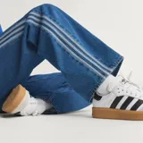 Pantalón Adidas Firebird de denim azul de corte holgado, con tiro medio y las icónicas tres tiras blancas a lo largo de los laterales de las piernas.