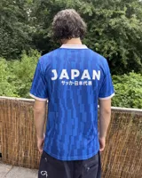 Camiseta de fútbol de manga corta en color azul con diseño estampado abstracto y cuello en V rosado con detalles blancos a juego con los puños. Presenta inscripciones y escudos deportivos en el pecho.