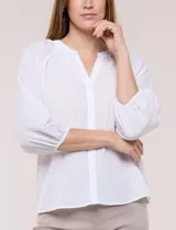 Blusa de gasa de color lila con calce holgado, cuello a la base con escote en V y cartera de botones a tono. Cuenta con fruncidos en el cuello y hombros que otorgan volumen, manga tres cuartos estilo abullonado con puño elastizado y ruedo suavemente redondeado.