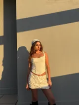 Conjunto de top corset con breteles finos y falda mini con lentejuelas, ambos color blanco.