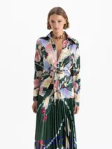 Camisa de satén con estampado multicolor, cuello camisero, mangas largas y puños con botones dorados. Cierre frontal oculto y lazos en la cintura para ajustar la silueta.