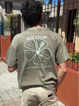 Remera verde militar de corte oversize con cuello redondo y estampado en la espalda con el logo de Brixton, una flor de hibisco y la frase "Where hibiscus grows, peace flows".
