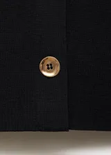 Chaleco de punto fino color negro, con cuello redondo, diseño recto sin mangas y cierre frontal de botones dorados.