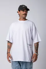 Remera blanca de corte oversize con cuello redondo y mangas cortas. Presenta un pequeño estampado tipográfico en la parte inferior frontal y un diseño gráfico de mayor tamaño en la espalda.