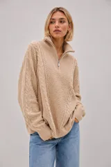 Sweater de punto grueso color beige, con diseño de trenzas y textura, cuello alto con cierre metálico frontal y calce oversize.