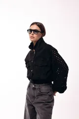 Campera de jean negra con mangas largas tejidas en crochet con diseño calado y detalles florales en relieve. Presenta cuello camisero, cierre frontal y bolsillos en el pecho.