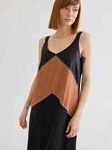 Vestido midi de corte recto y escote en V, con diseño bicolor que combina paneles en negro y tostado en forma de V invertida. Presenta costuras decorativas visibles en la unión de los colores.