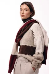 Sweater de tejido de punto grueso con diseño de bloques de color en tonos beige, marrón y bordó. Presenta un corte relajado, mangas amplias y detalles de costuras visibles en contraste que separan las franjas de color.