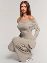 Vestido largo de punto acanalado en color beige, con diseño de hombros descubiertos y cuello solapado. Presenta mangas largas y un corte ajustado al cuerpo.