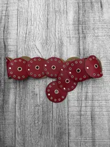 Faja de cuero bordó con apliques circulares y ojalillos metálicos.