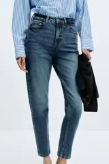 Jeans de mujer, tiro alto, corte Mom Fit con pierna slim y largo tobillero. Denim azul medio con efecto desgastado y lavado. Presenta cinco bolsillos y cierre frontal con cremallera y botón.