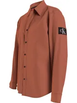 Camisa color ladrillo de corte relaxed, confeccionada en sarga de algodón elástico. Tiene cuello en punta, cierre de botones, puños redondos y bajo recto.