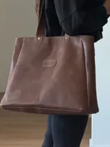 Bolso tipo tote grande confeccionado en cuero vacuno color marrón, con cierre superior, bolsillo interno y gancho para llaves.