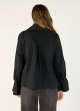 Chaqueta color tostado de corte recto y diseño cruzado con doble botonadura frontal. Presenta cuello solapa y mangas largas con puños acampanados y fruncidos.