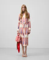 Vestido camisero midi con estampado abstracto en tonos rosa, azul y blanco. Tiene cuello camisero, mangas largas con puños, cinturón de lazo y bolsillos laterales.