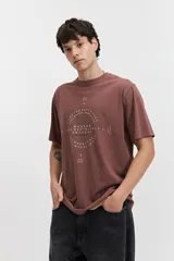 Remera de manga corta color marrón, con ajuste regular y escote redondo. Presenta un estampado frontal con texto en blanco formando un diseño circular.