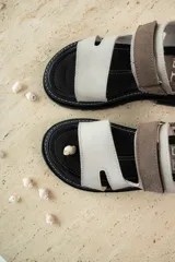 Sandalias de cuero marrón con diseño de tiras anchas y ajuste mediante velcro. Presentan una plantilla acolchada color tostado con detalles en rojo y una suela de goma negra con plataforma dentada.