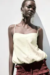 Top corto color crema confeccionado con lino, escote pico y tirantes finos. Detalle de espalda abierta con tira elástica horizontal y bajo abullonado con elástico interior.