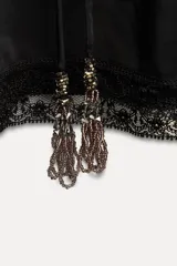 Vestido corto negro con cuello redondo, mangas largas abullonadas con puños elásticos y detalle de encaje y bordados con abalorios. Incluye lazo para ajustar en la cintura.