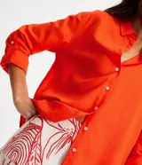 Camisa de manga larga color verde lima, con cuello camisero y botonadura frontal. Presenta un dobladillo trasero más largo que el delantero.