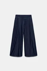 Pantalón tipo culotte de tiro alto confeccionado en denim azul oscuro. Presenta pinzas delanteras, pernera ancha y corta, bolsillos laterales ocultos y cierre frontal con cremallera, botón y ganchos.