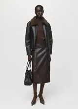 Chaqueta de efecto piel en color negro con diseño oversize, cuello camisero y forro interior de borreguito marrón. Cuenta con cierre delantero con cremallera, dos bolsillos de parche laterales y manga larga.