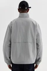 Campera rompevientos de nylon color gris, repelente al agua, con cuello elevado, cierre frontal y bolsillos laterales con botón a presión oculto.
