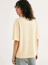 Camiseta color crema de corte amplio con estampado de paisaje costero enmarcado por columnas y la frase "Blue Horizon" en celeste.