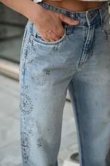 Jean de tiro alto y corte recto, color azul claro con efecto gastado, adornado con tachas plateadas brillantes formando diseños en los laterales.