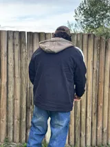 Campera de pana negra con capucha incorporada, bolsillos laterales y cierre frontal con botones a presión y cremallera.