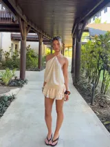 Vestido corto color crema, con escote halter, espalda descubierta y falda con volados.