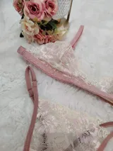 Conjunto de lencería compuesto por bralette y tanga regulable, confeccionado en encaje color champagne con detalles florales bordados en hilo rosado y terminaciones en cinta color rosa viejo.