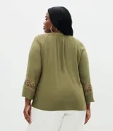 Blusa de viscosa color verde oliva, con cuello redondo, lazo con borlas decorativas y mangas largas con bordado étnico en los puños.