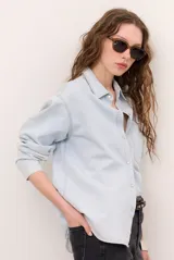 Camisa de jean de corte oversize, color celeste claro, con cierre frontal de broches metálicos y un bolsillo aplicado en el pecho.