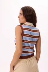 Top tejido sin mangas con diseño a rayas horizontales en tonos azul marino, celeste y crema. Presenta cuello tipo polo con tapeta de botones frontal y terminaciones acanaladas en el ruedo y sisas.
