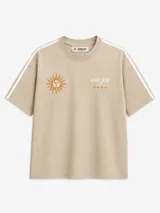 Remera oversize de color beige con diseño bordado de un sol y estrellas, texto "BHN DSG" y bandas blancas en las mangas.